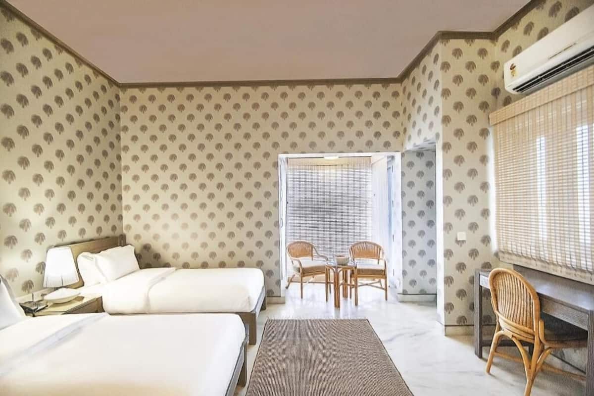 Une chambre d’hôtel avec deux lits, un coin repas avec des chaises et un appareil de climatisation.