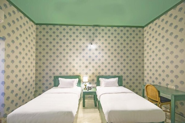 A room with two single beds, a small table with a lamp, and a chair. - Sonaar Haveli Jaislamer (Jaisalmer)
