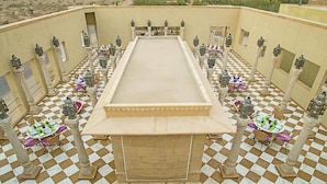 Un sol à carreaux avec une piscine centrale, entourée de tables et de chaises, ainsi que de lanternes décoratives.