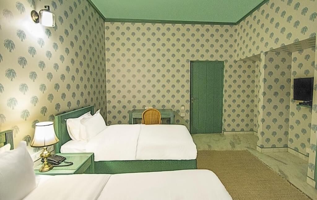 A hotel room with a bed, a nightstand, a lamp, a chair, and a television.