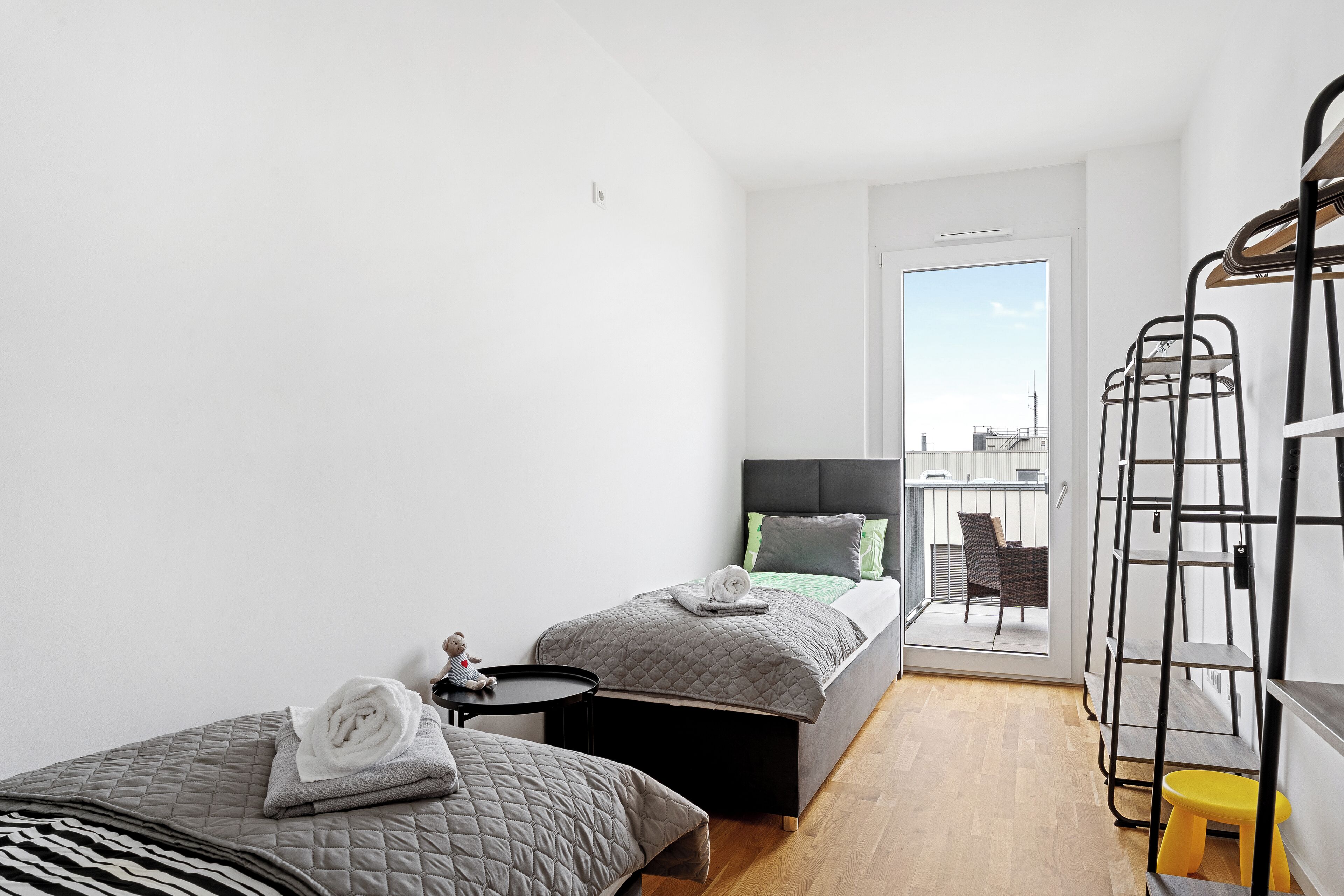 Ein modernes, minimalistisches Schlafzimmer mit zwei Betten, einem Balkon und einer Metallleiter.