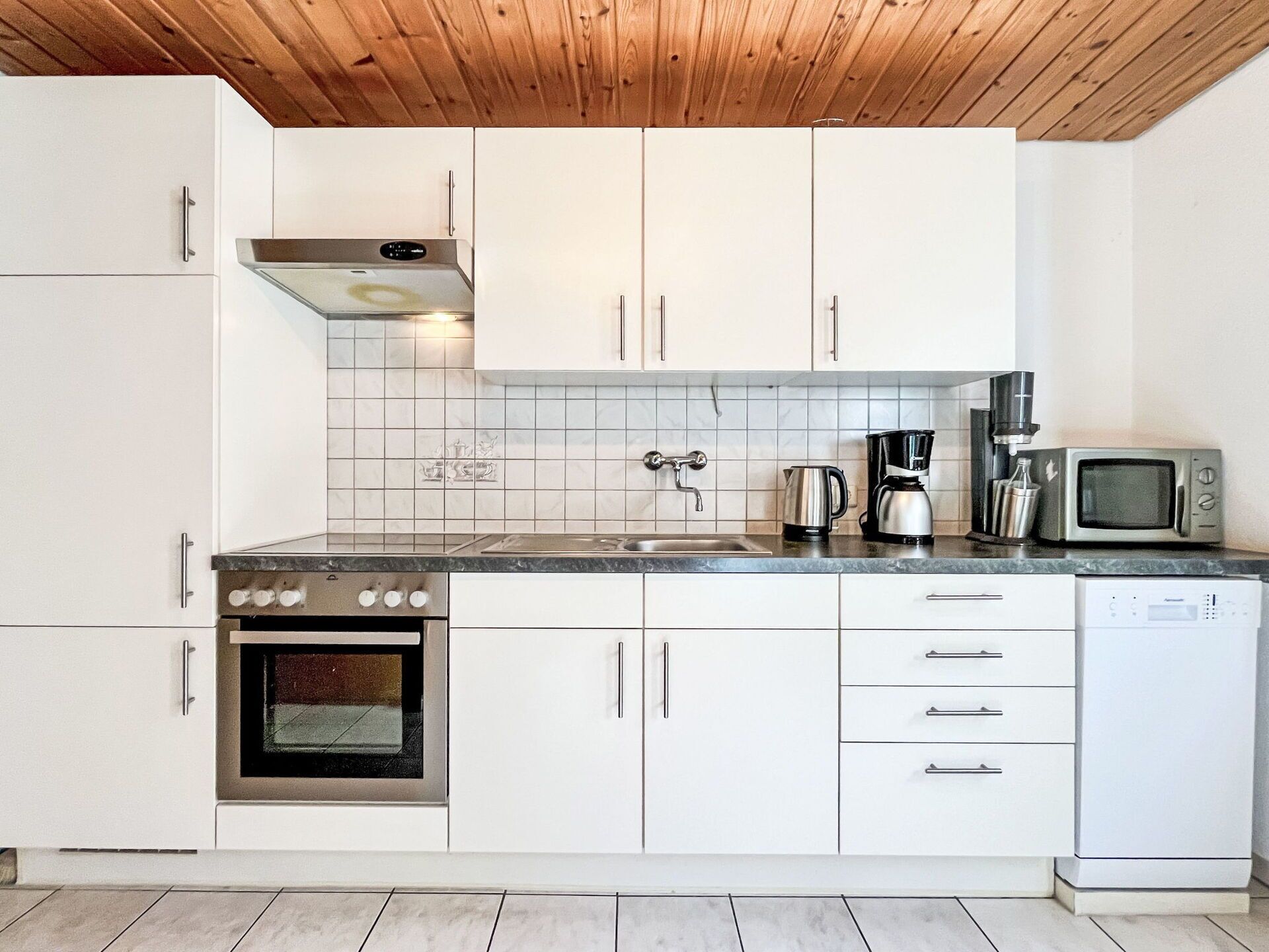 Cucina moderna con mobili bianchi, piano cottura in acciaio inox, microonde e macchina del caffè.