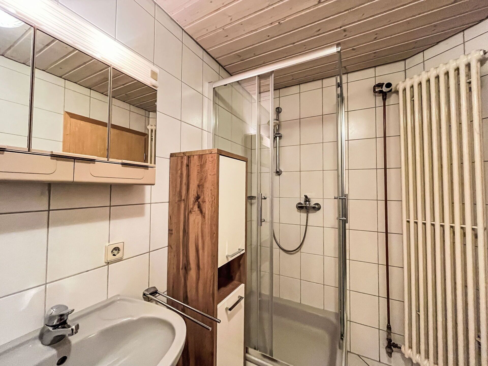 Une salle de bain équipée d’un lavabo, d’un miroir, d’un meuble en bois, d’une douche et d’un radiateur.