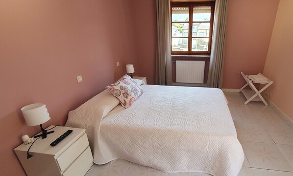 A neatly made bed with a white quilt, a bedside lamp, and a remote control on a nightstand. - Casa Rural Nito (Villayon)