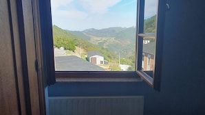 A room with a window overlooking a hilly landscape with buildings and wind turbines. - Casa Rural Nito (Villayon)