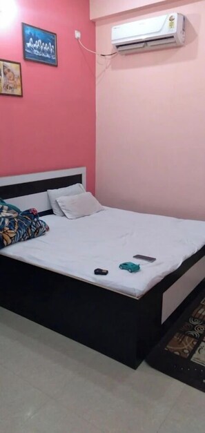 A room with a bed, a wall-mounted air conditioner, and a painting. - suvidha guest house (Varanasi)