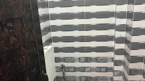A bathroom with a striped tile wall, a toilet, a pink bucket, and a white basin. - suvidha guest house (Varanasi)