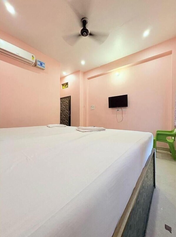 A hotel room with a single bed, a ceiling fan, an air conditioning unit, a flat-screen TV, and a green chair.
