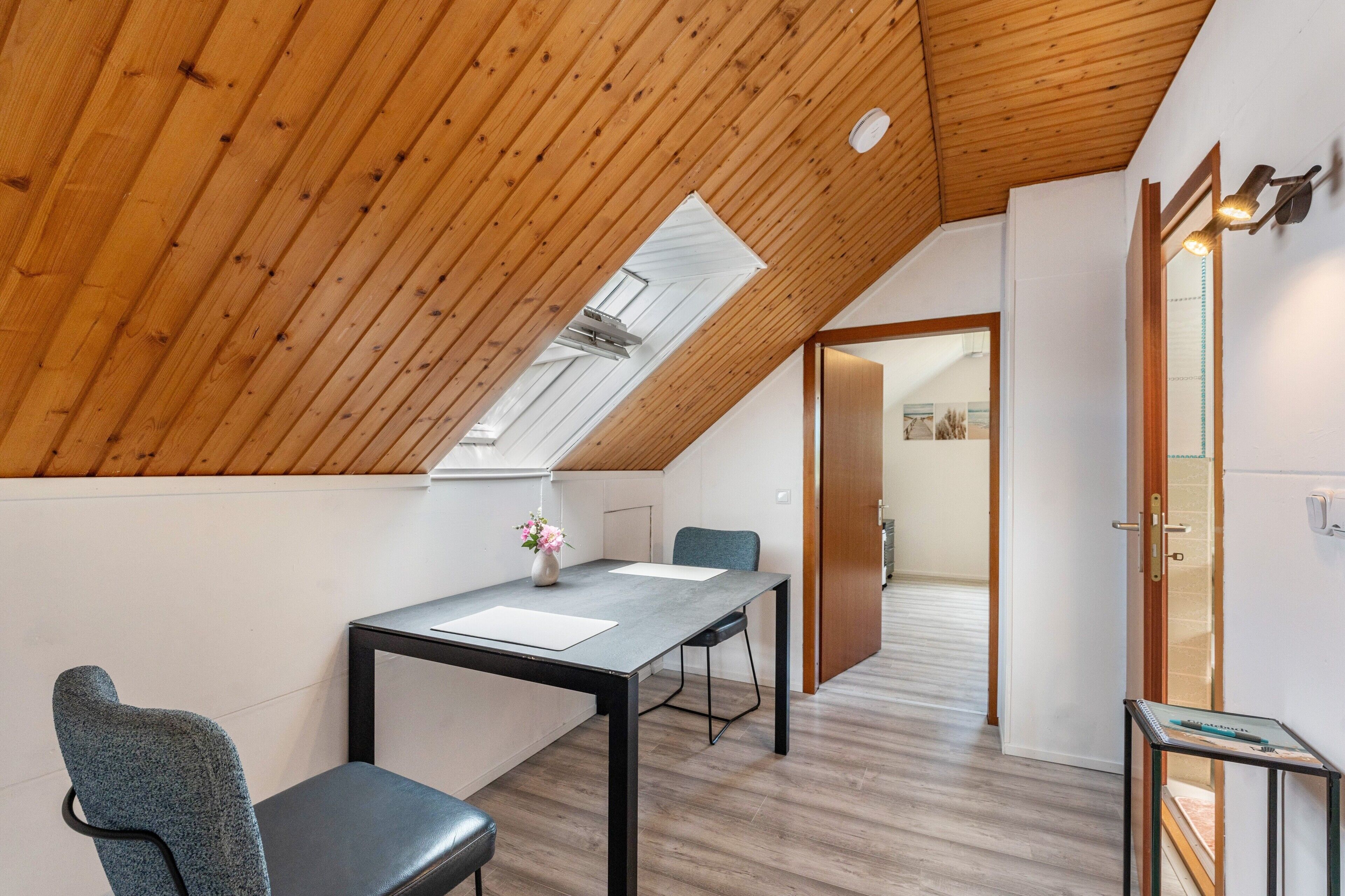 Una habitación con techo inclinado, tragaluces, una mesa de comedor con sillas y una mesita auxiliar.
