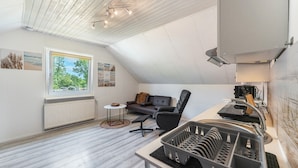 Una habitación moderna estilo loft con techo inclinado, comedor con mostrador de cocina, silla de oficina negra, sofá y una pequeña mesa redonda.