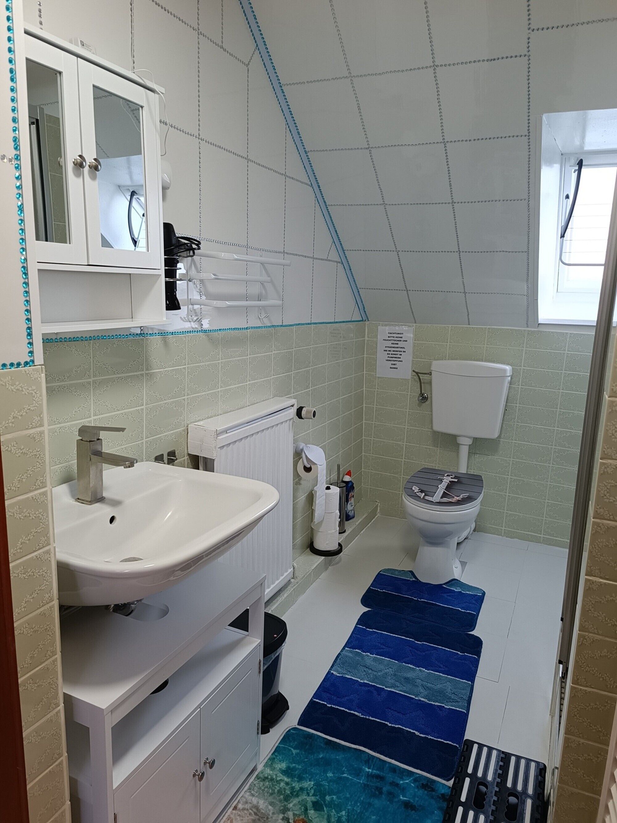 A bathroom with a white sink, a toilet, a shower area, and a blue striped bath mat.