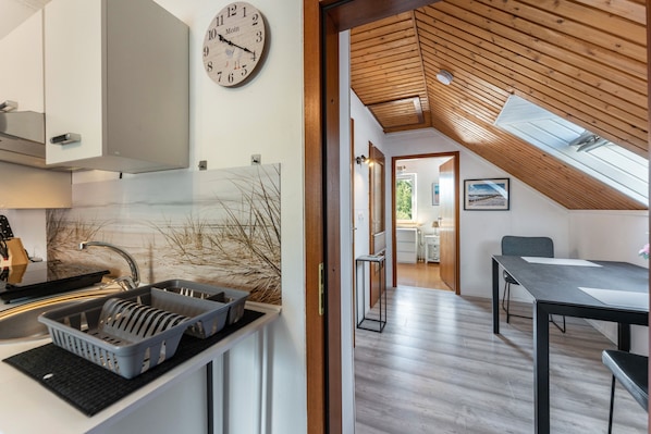 A modern kitchen with a clock, a dining area with a table and chairs, and a view of the outdoors through a skylight.