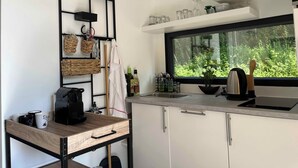 Una cocina moderna con estufa integrada, ventana con vistas a la vegetación y estante con utensilios de cocina.