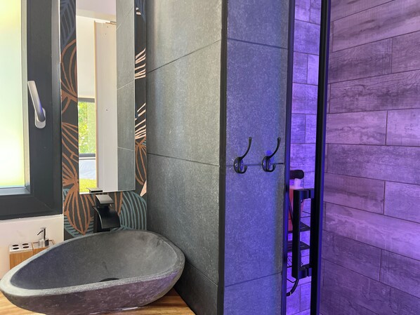 A bathroom with a stone sink, a mirror, and a door with hooks.