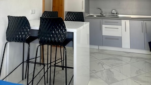 Una cucina moderna con mobili grigi, un piano di lavoro bianco e un lavello. Sono presenti due sedie nere con motivo a diamante.