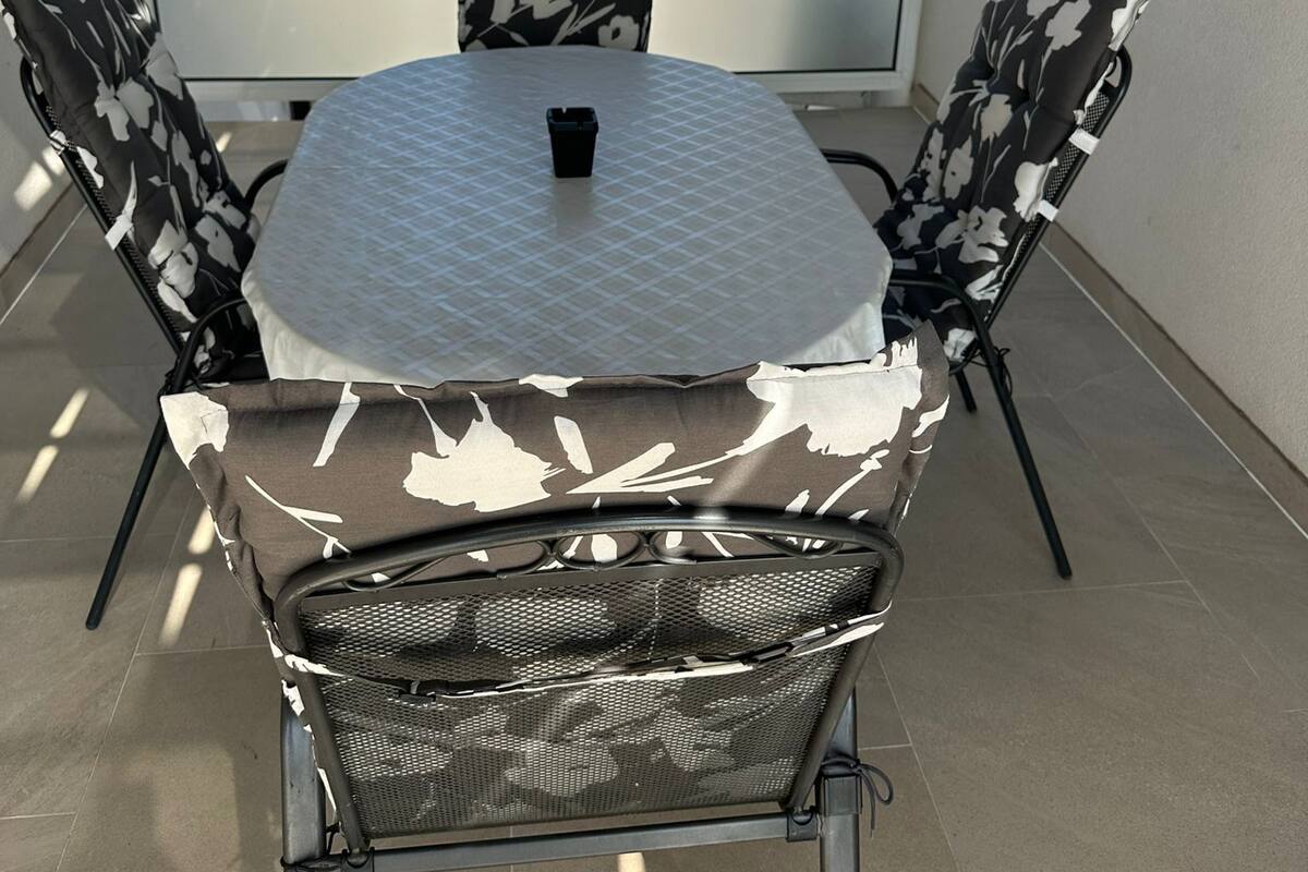 A small outdoor patio with a round table and four chairs, a black mesh chair, and a white tablecloth.