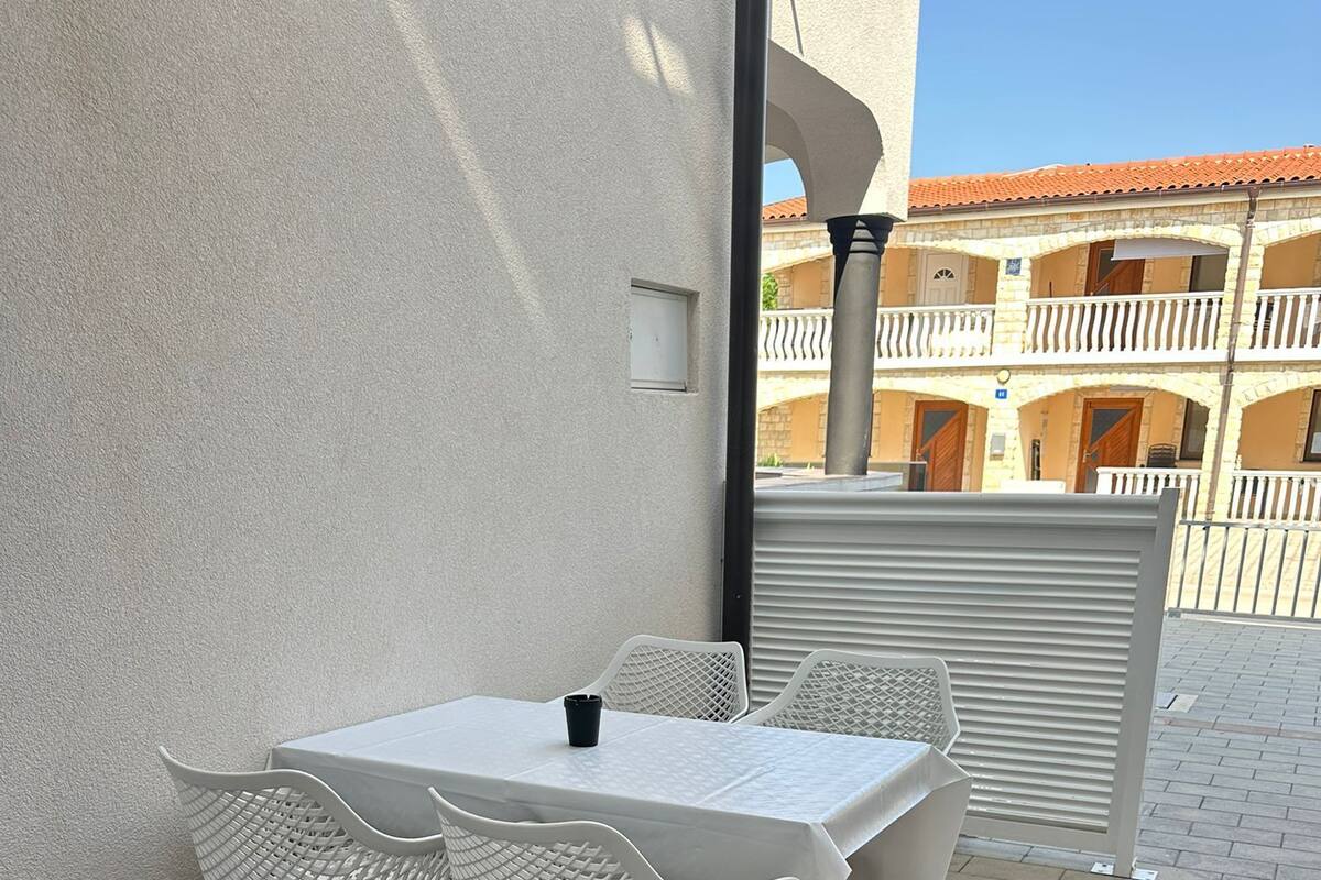 A white outdoor table with four chairs, a black cup, and a metal railing in the background.