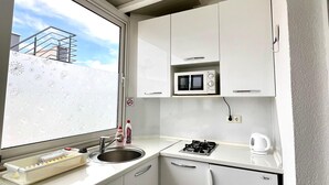 Una cucina compatta con mobili bianchi, un forno a microonde, un fornello a gas e un lavello.