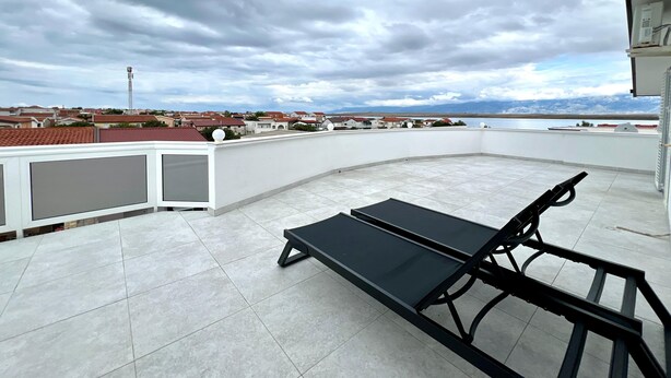 Una terrazza sul tetto con una poltrona da relax nera, un muro bianco e vista su una zona residenziale e montagne all'orizzonte.