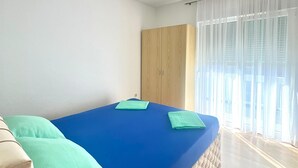 Una stanza con un materasso blu, un armadio in legno e una finestra con tende leggere.