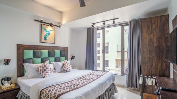 Una habitación de hotel moderna con una cama grande, cabecera de madera, televisor de pantalla plana, escritorio con control remoto y vista al exterior a través de una puerta corredera de vidrio.