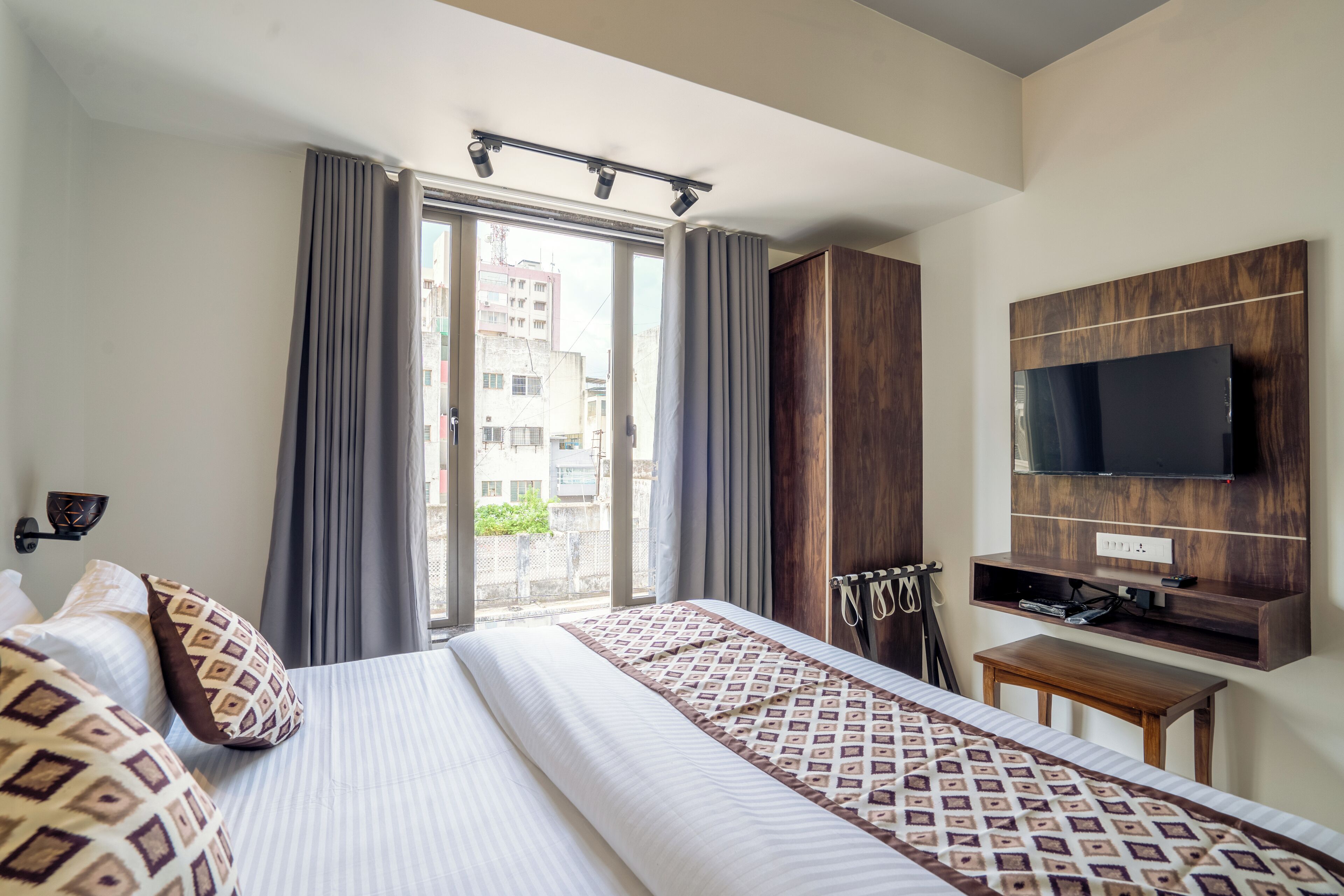 Habitación de hotel con una cama grande, televisión montada en la pared, una mesita pequeña y una ventana con cortinas.