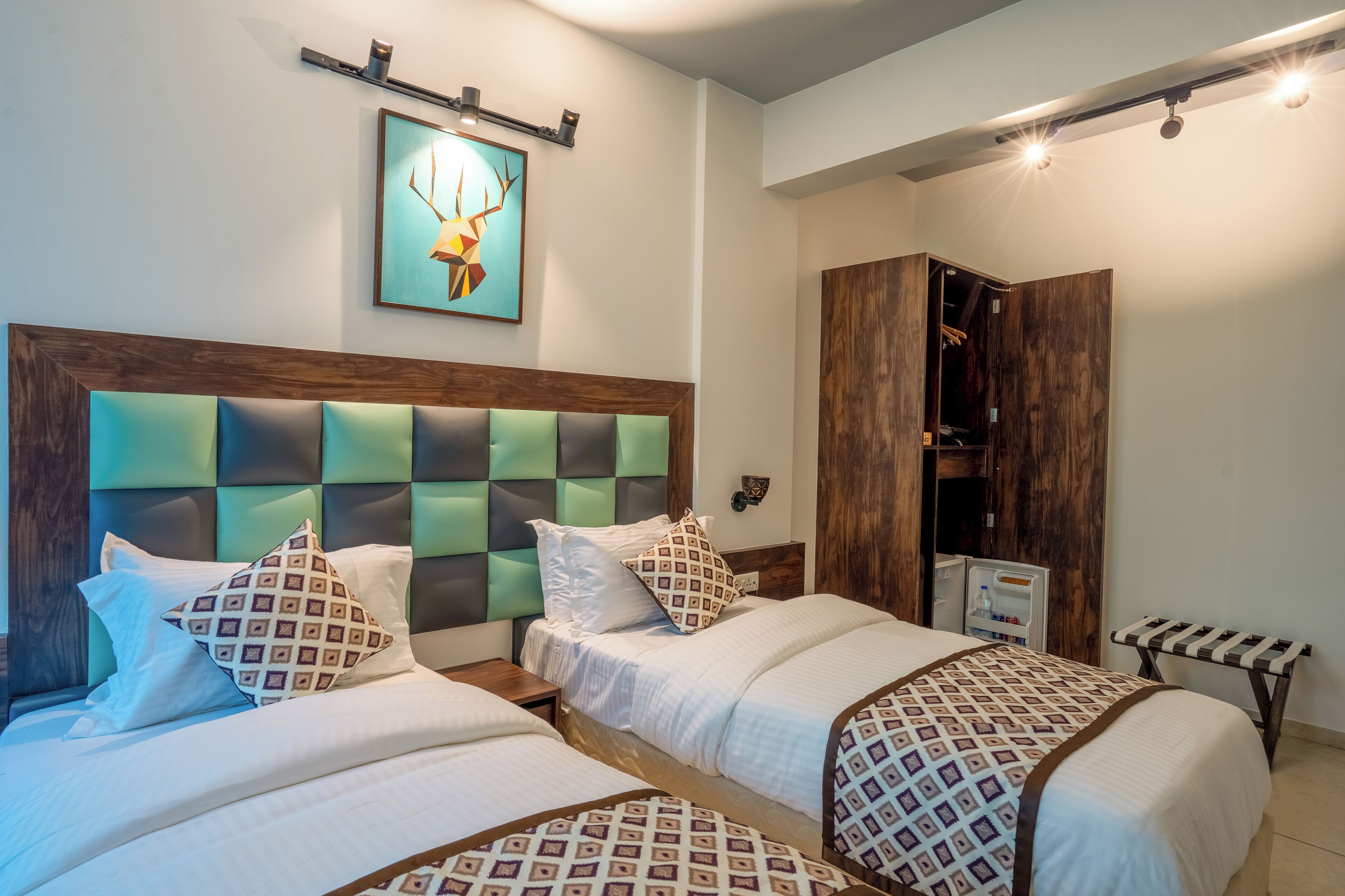 A hotel room with two beds, a wooden headboard, a framed artwork, a wardrobe, and a bench.