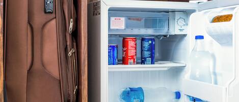 A compact refrigerator with a water bottle, a can of Coca-Cola, and a can of Pepsi.