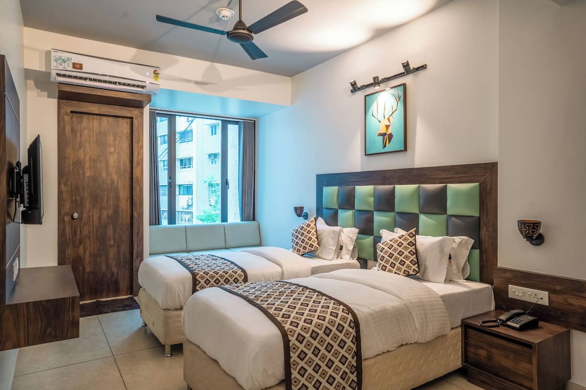 A hotel room with two beds, a ceiling fan, an air conditioning unit, a window with a view, and a painting on the wall.