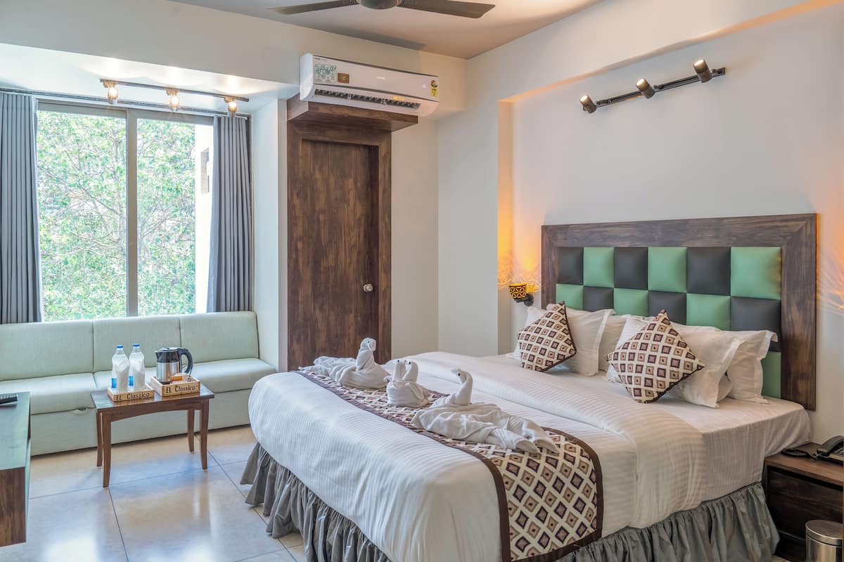 A hotel room with a bed, a sofa, an air conditioner, and a window with curtains.