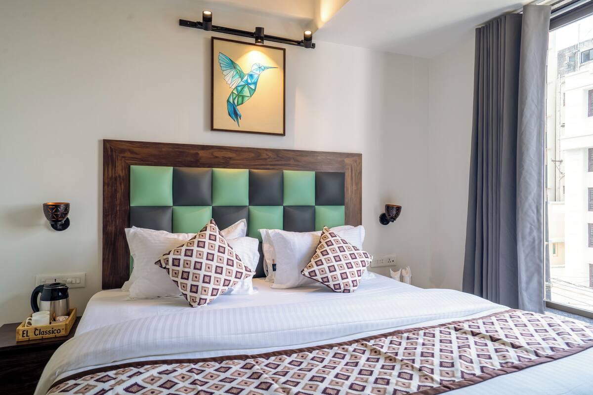 A neatly made bed with patterned pillows, a framed artwork above, and a coffee maker on the nightstand.