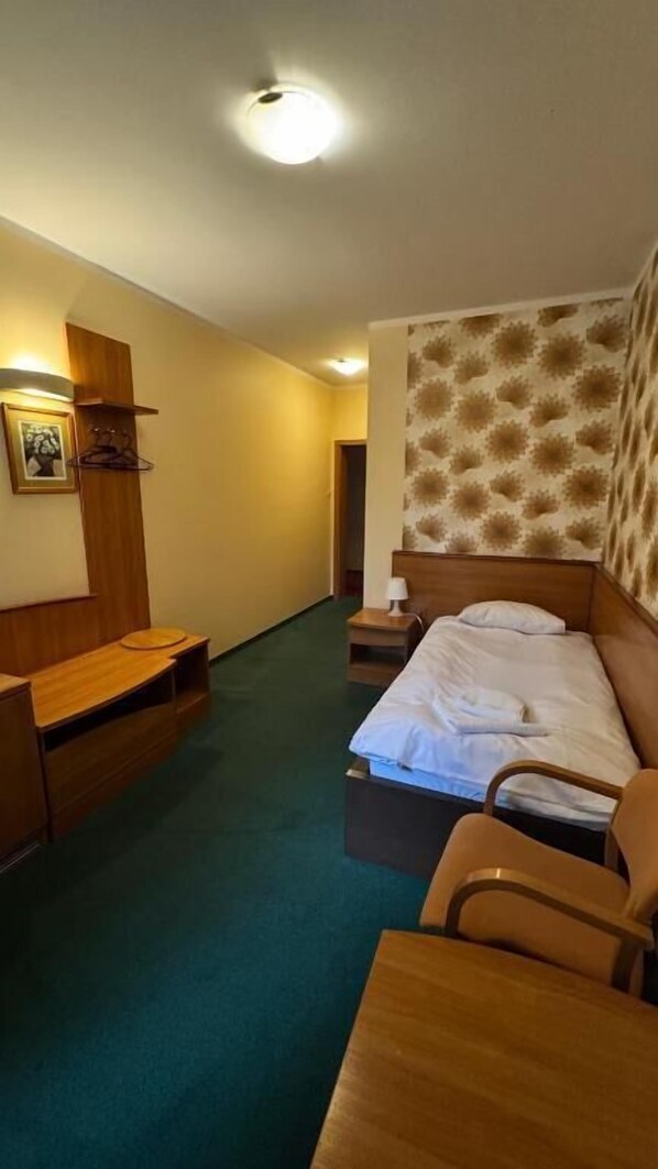 A hotel room with a bed, a wooden desk, a chair, a nightstand, and a wall-mounted lamp. - Bobrowy Resort (gmina Zabludow)