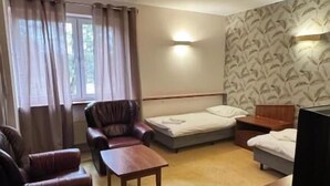 Une chambre d’hôtel avec un canapé, une petite table, un lit, une télévision et une fenêtre avec des rideaux.