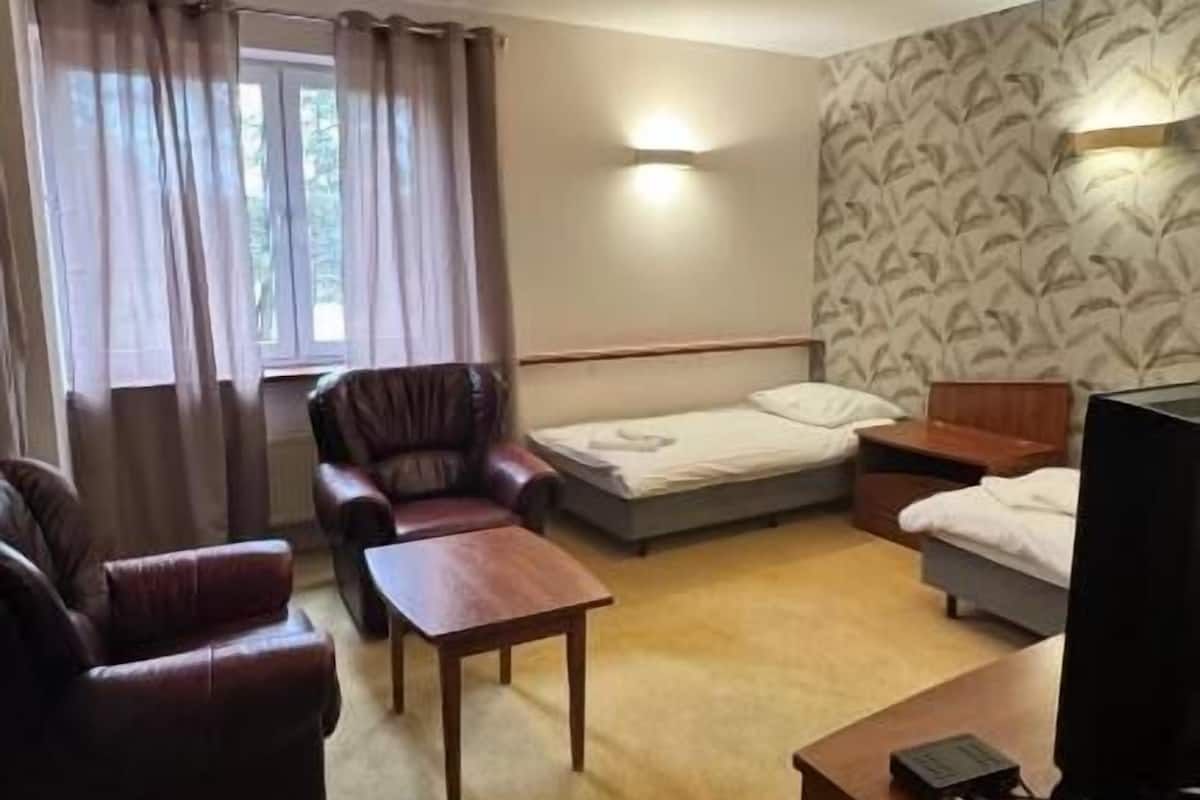 Ein Hotelzimmer mit einer Couch, einem kleinen Tisch, einem Bett, einem Fernseher und einem Fenster mit Vorhängen.