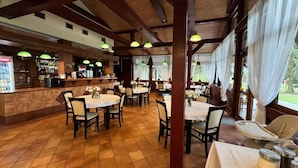 Un restaurant avec des poutres en bois, des suspensions vertes et un coin bar. Les tables sont disposées pour accueillir les clients, et une chaise haute pour bébé est à disposition.