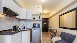 A compact kitchen with a built-in microwave, a refrigerator, and a stove. There is a small dining area with a table and chairs, and a sofa in the living area. - Queen Studio, City View - Virgo Nest Rentals (Cebu City)