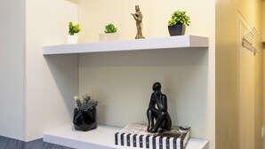A white shelf with decorative items, including a black sculpture, a book, and small potted plants. - Queen Studio, City View - Virgo Nest Rentals (Cebu City)