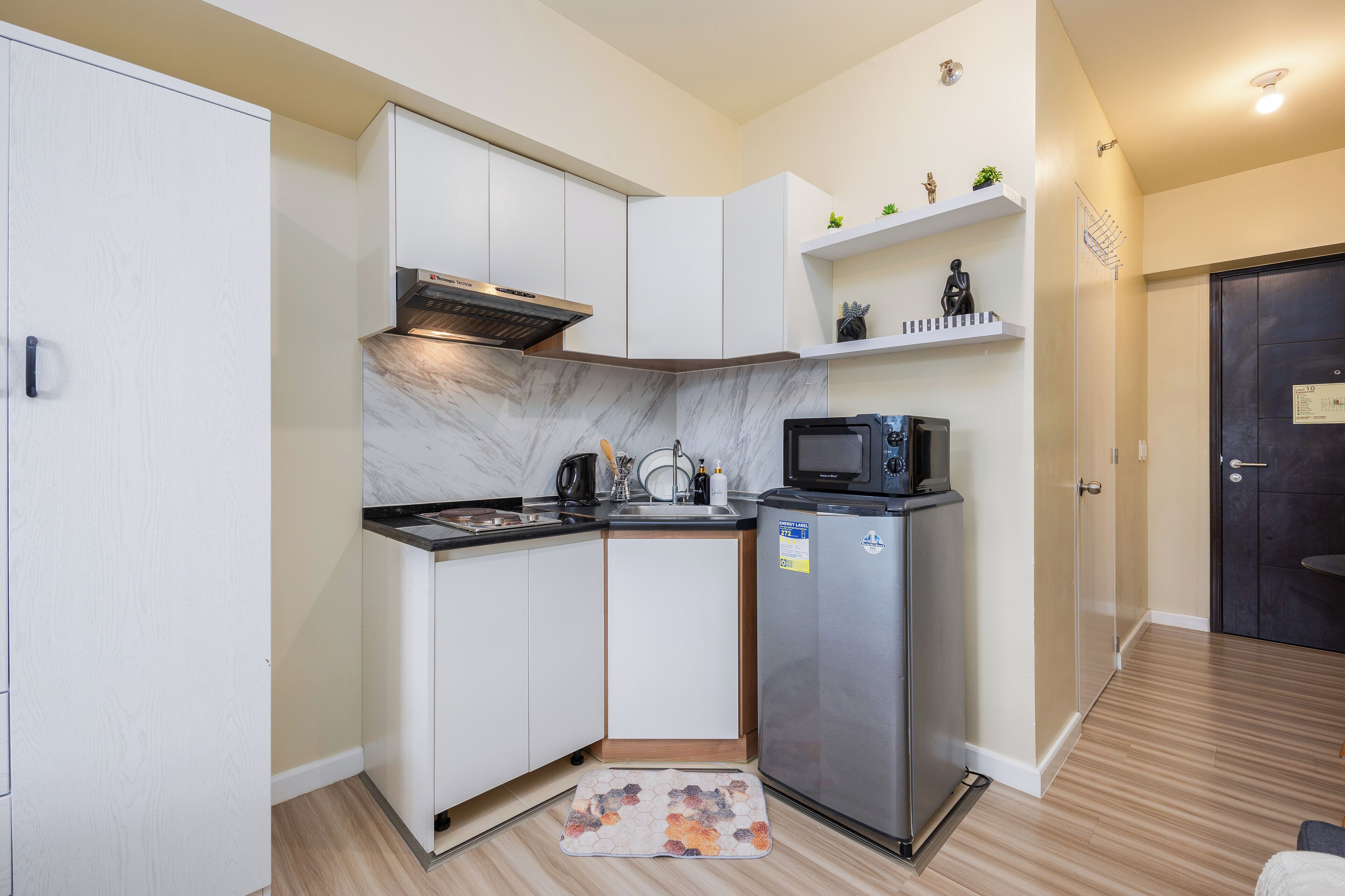 A compact kitchen with white cabinets, a stainless steel refrigerator, a microwave, and a built-in oven.