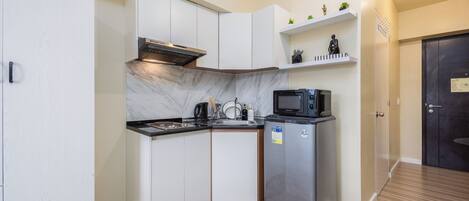 A compact kitchen with white cabinets, a stainless steel refrigerator, a microwave, and a built-in oven.