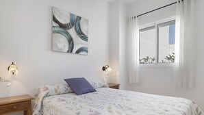 Une chambre à coucher comprenant un lit, deux tables de chevet, un tableau abstrait accroché au mur et une fenêtre avec des rideaux.