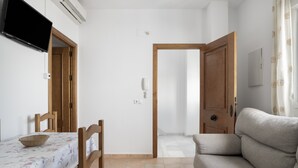 Une pièce comprenant une table à manger, des chaises, un canapé, un téléviseur et une porte donnant sur une autre pièce.