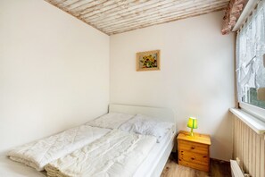Une chambre à coucher avec un lit, une table de chevet avec une lampe, une fenêtre ornée de rideaux en dentelle et un tableau accroché au mur.