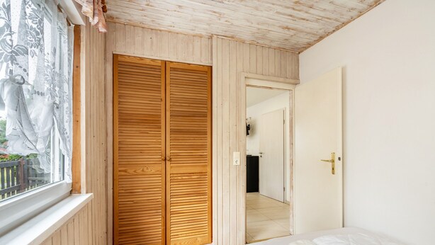 A bedroom with a wooden wardrobe, a bed, and a window with curtains.