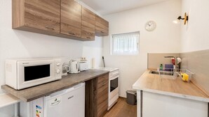A compact kitchen with wooden cabinets, a microwave, a toaster, a kettle, and a sink with a dish rack.