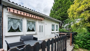 A white building with a tiled roof, a wooden fence, and a patio with outdoor furniture.