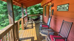 Een houten veranda met een hangmat, een schommelstoel en een bankje. Een bord met de tekst 'Welcome to Our Porch' is zichtbaar.