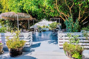 An outdoor seating area with thatched umbrellas, white furniture, and potted plants. - Kamarela Studios (Kamari)