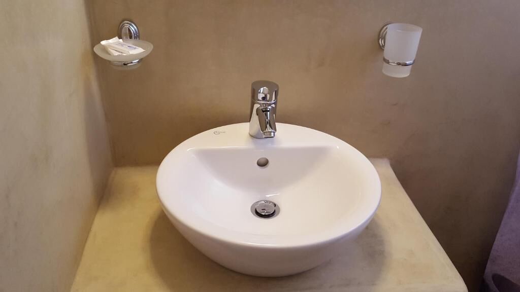 Een wastafel met een chromen kraan, een zeepbakje en een glazen beker aan de muur.