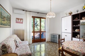 Una habitación con cama, una silla, un escritorio, un radiador, una ventana con cortinas y un aire acondicionado de pared.