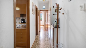 Un couloir étroit avec des armoires en bois, un sol carrelé, un porte-manteau et un luminaire suspendu.